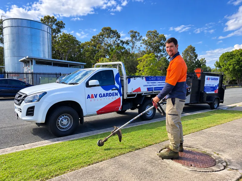 Amos from A&V Garden Solutions whipper snipping a verge beside the branded work ute and trailer