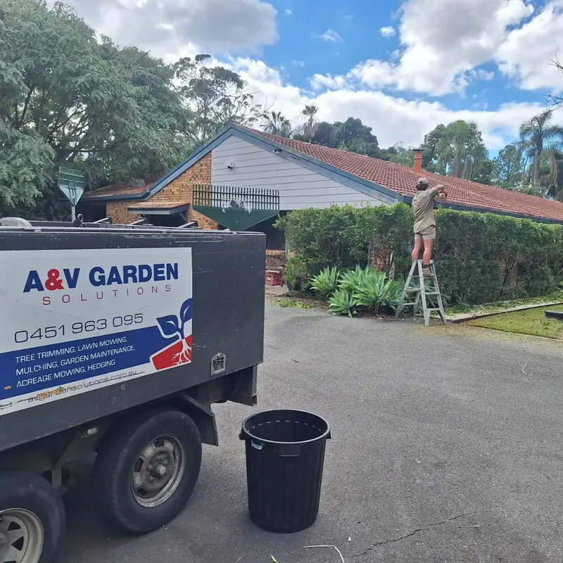 A&V Garden Solutions trailer parked on site while a team member trims hedges
